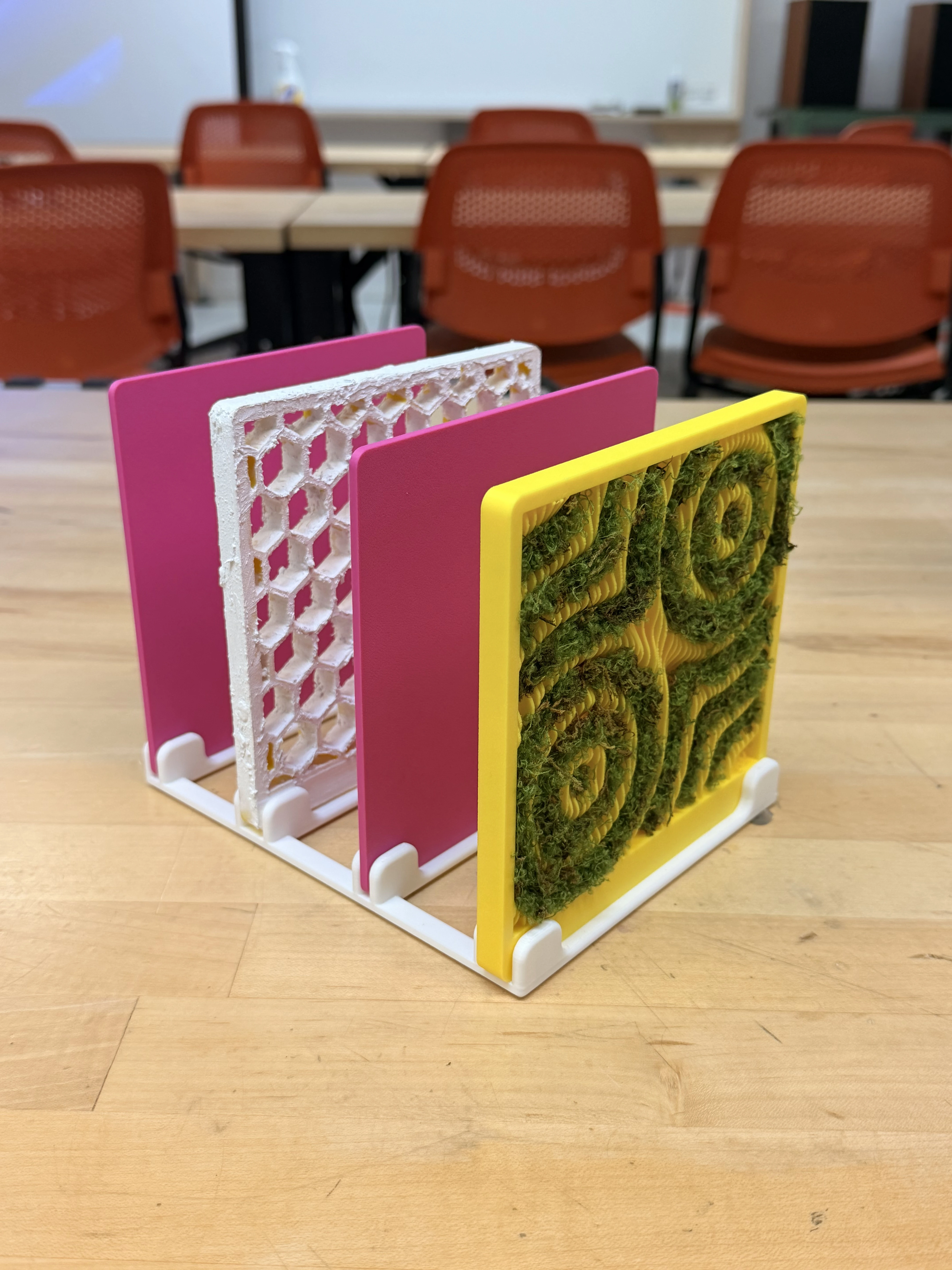 Final prototype: pink, white hexagonal-lattice and yellow moss panels standing in a 3D-printed rack