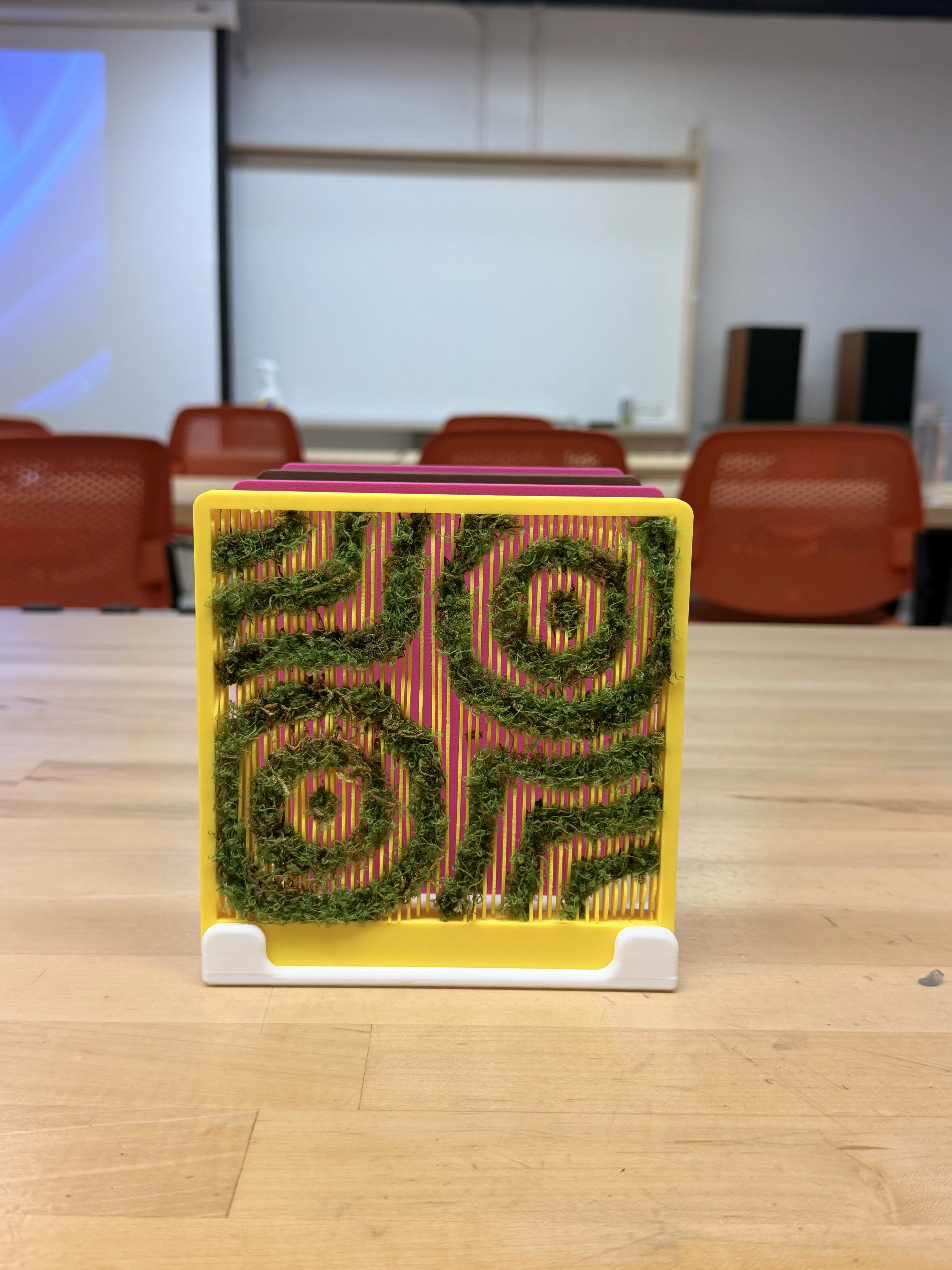 Final prototype, front view: yellow-framed panel with moss set in swirling grooves
